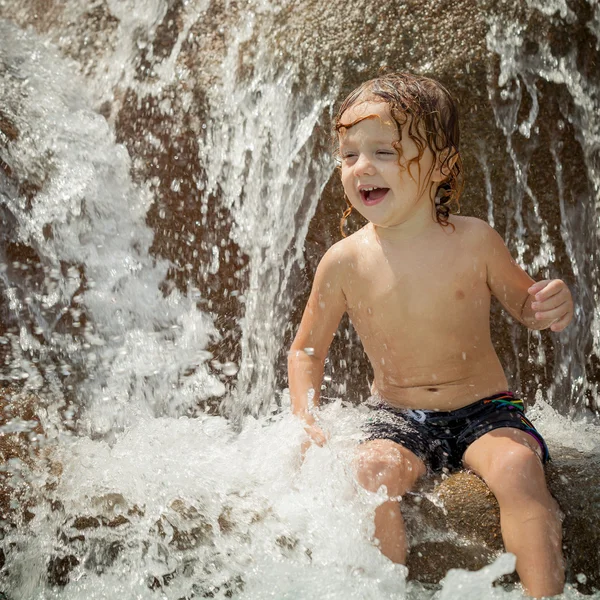 Ευτυχής μικρό αγόρι κάθεται δίπλα στην πισίνα στο πάρκο με τις νεροτσουλήθρες — Φωτογραφία Αρχείου
