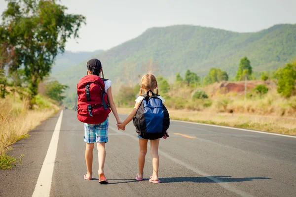 Two little girls with backpack walking on the road — Stock Photo, Image