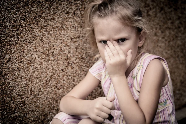Porträtt av en ledsen liten flicka som sitter nära väggen — Stockfoto