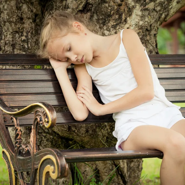 Retrato de un niño triste sentado en un banco en el parque debajo de —  Fotos de Stock