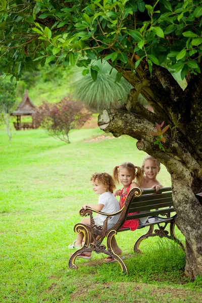 Crianças felizes sentadas no banco perto da árvore — Fotografia de Stock