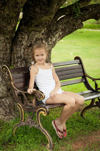 Menina feliz sentado no banco perto da árvore — Fotografia de Stock