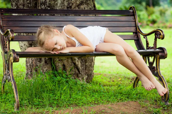 Portrait of a sad child lying on a bench in the park under the — Stock Photo, Image