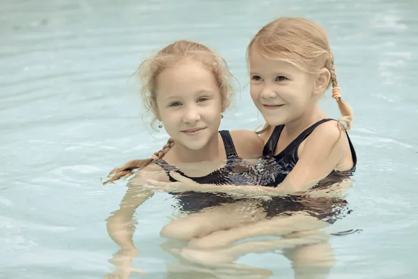 Twee gelukkige kleine meisjes spelen rond in het zwembad — Stockfoto