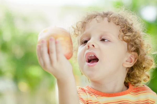 Little boy standing on the grass and holding apple — Stock Photo, Image