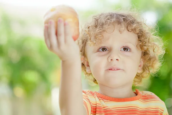 Kleiner Junge steht auf dem Gras und hält Apfel — Stockfoto