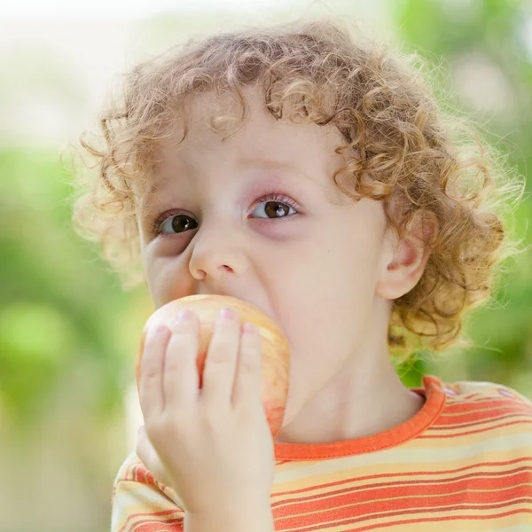 Little boy standing on the grass and holding apple — Stock Photo, Image