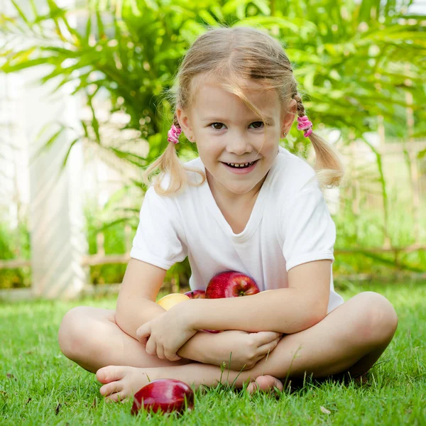 Petite fille assise sur l'herbe et tenant des pommes — Photo