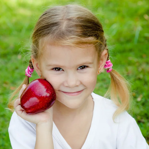 Petite fille assise sur l'herbe et tenant des pommes — Photo