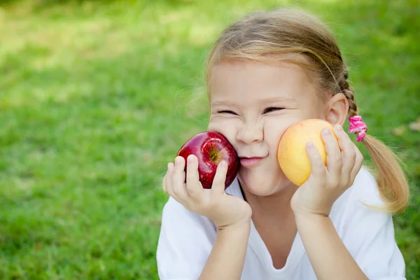 Bambina seduta sull'erba e con le mele in mano — Foto Stock