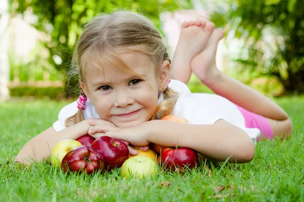 Petite fille couchée sur l'herbe et tenant des pommes — Photo