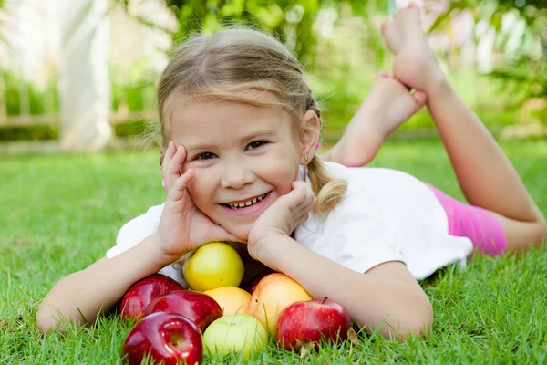 Kleines Mädchen auf dem Gras liegend und Äpfel haltend — Stockfoto