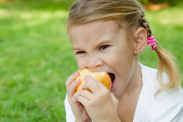 小さな女の子は草の上に座っているとリンゴを保持 — ストック写真