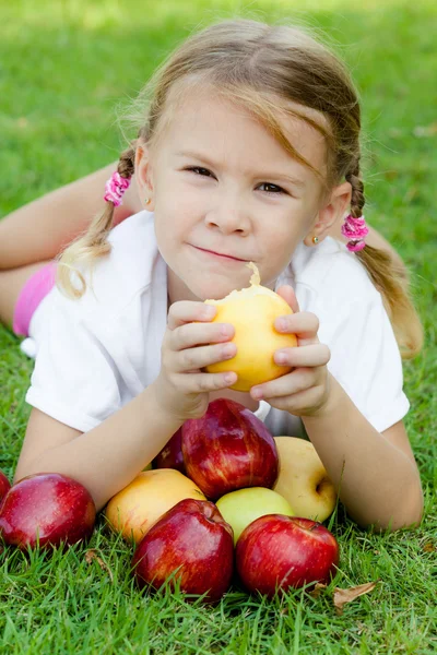 Little girl lying on the grass and holding apples — Stock Photo, Image
