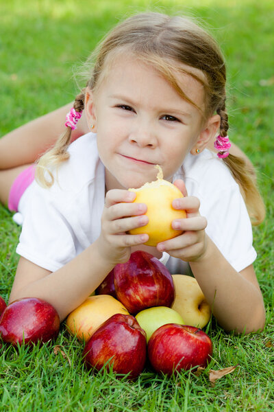 little girl lying on the grass and holding apples