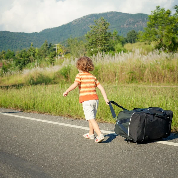 Niño pequeño con una bolsa grande va en el camino durante el día — Foto de Stock