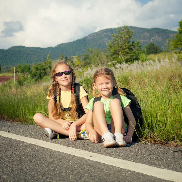 Две девушки с рюкзаками сидят на дороге — стоковое фото