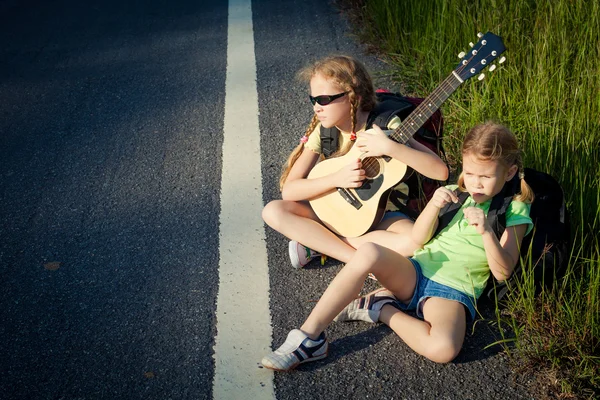 Dos chicas con mochilas sentadas en la carretera —  Fotos de Stock