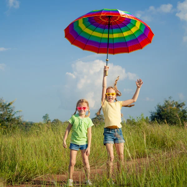 Twee meisjes springen op de weg met een paraplu — Stockfoto