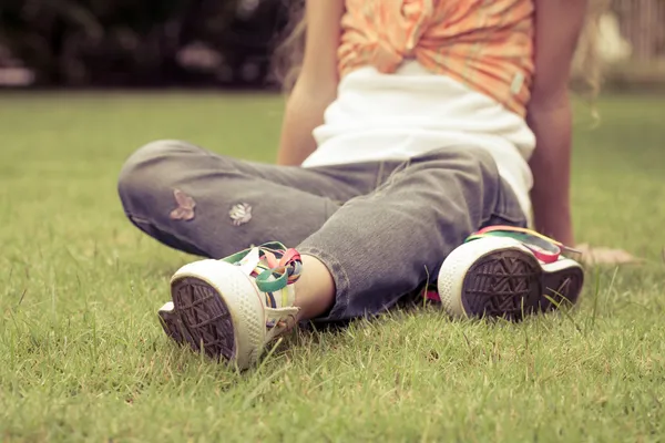 Weiße Turnschuhe auf Mädchenbeinen im Gras im sonnigen, heiteren Sommer — Stockfoto