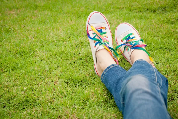 Weiße Turnschuhe auf Mädchenbeinen im Gras im sonnigen, heiteren Sommer — Stockfoto