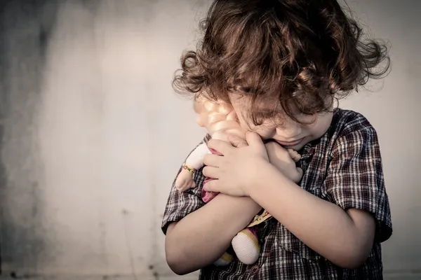 Triste niño abrazando a una muñeca —  Fotos de Stock