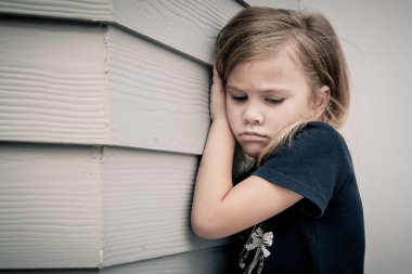 Portrait of sad little girl sitting near  wall in the day time