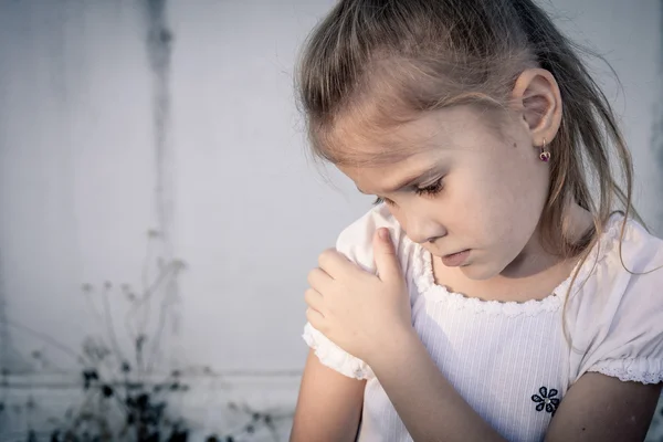 Retrato de uma menina triste sentada perto da parede durante o dia — Fotografia de Stock