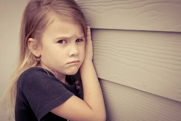 Retrato de una niña triste sentada cerca de la pared durante el día — Foto de Stock