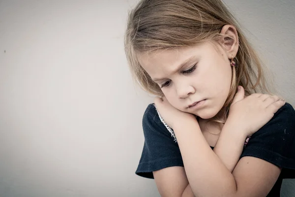 Porträtt av ledsen liten flicka sitter nära väggen under dagarna — Stockfoto