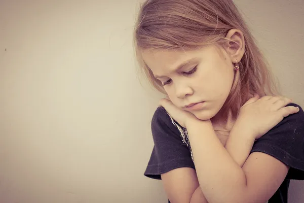 Retrato de uma menina triste sentada perto da parede durante o dia — Fotografia de Stock