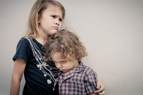 Portrait of sad little girl and little boy standing near wall in — Stock Photo, Image