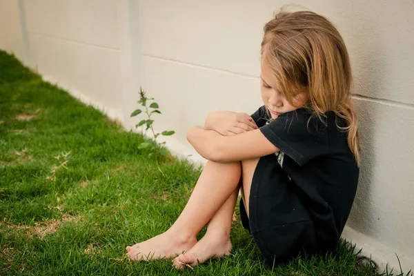 Retrato de una niña triste sentada cerca de la pared durante el día — Foto de Stock