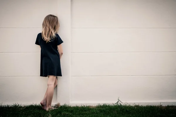 Портрет грустной маленькой девочки, стоящей у стены днем — стоковое фото