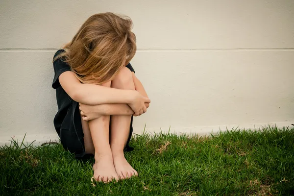 Портрет грустной маленькой девочки, сидящей у стены днем — стоковое фото