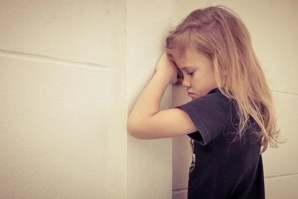Портрет сумної маленької дівчинки, що стоїть біля стіни вдень — стокове фото
