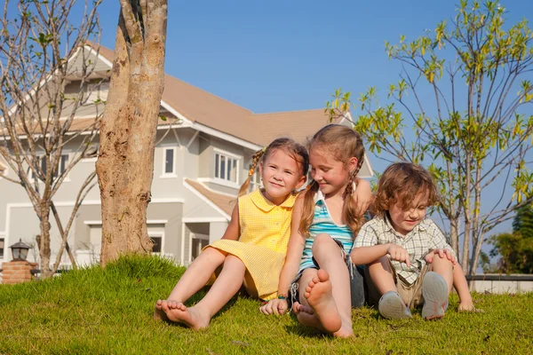 Zwei glückliche Mädchen und ein kleiner Junge sitzen in der Nähe des Hauses — Stockfoto