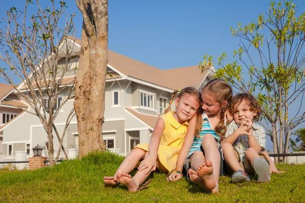 Zwei glückliche Mädchen und ein kleiner Junge sitzen in der Nähe des Hauses — Stockfoto