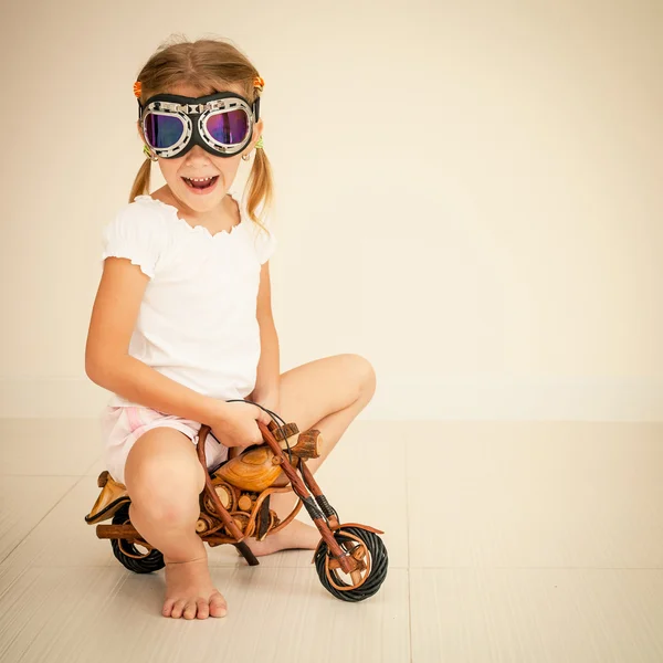 Little girl in glasses on toy motorcycle — Stock Photo, Image