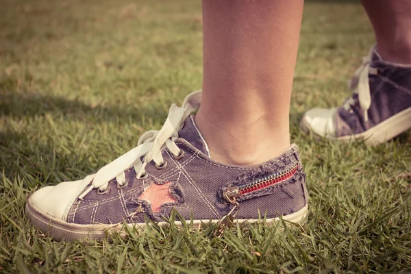 Baskets jeunes sur les jambes de la fille sur l'herbe pendant l'été serein ensoleillé — Photo