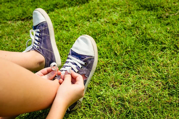 Zapatillas de deporte juveniles en piernas de chica en la hierba durante el soleado verano sereno — Foto de Stock