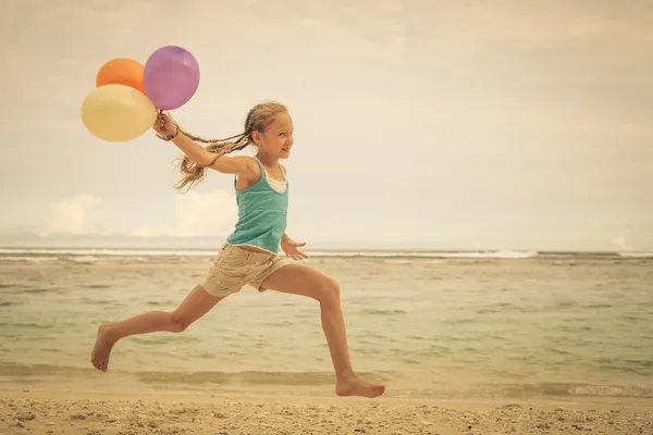 Menina com balões pulando na praia na costa azul do mar em su — Fotografia de Stock