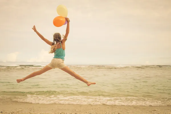 Chica con globos saltando en la playa en la orilla azul del mar en su —  Fotos de Stock