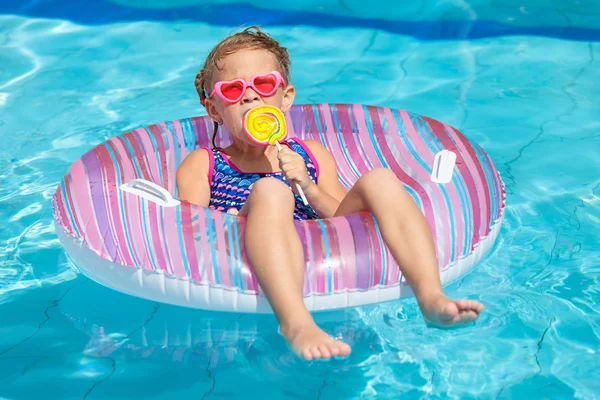 Liten flicka med lollipop liggande på uppblåsbara gummi cirkeln — Stockfoto