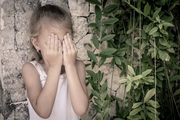Portrait of sad little girl standing near stone wall in the day — Stock Photo, Image