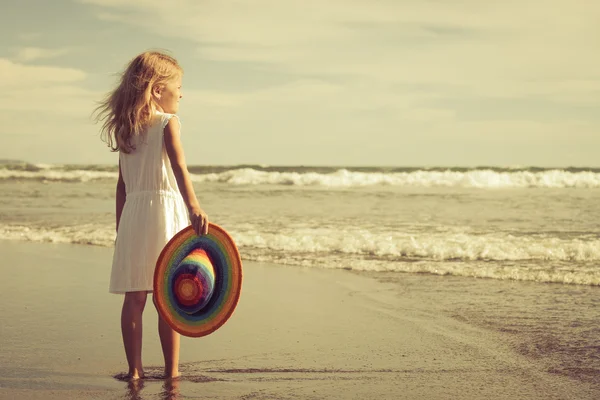 Glad liten flicka i hatten promenerar på stranden i dag tim — Stockfoto