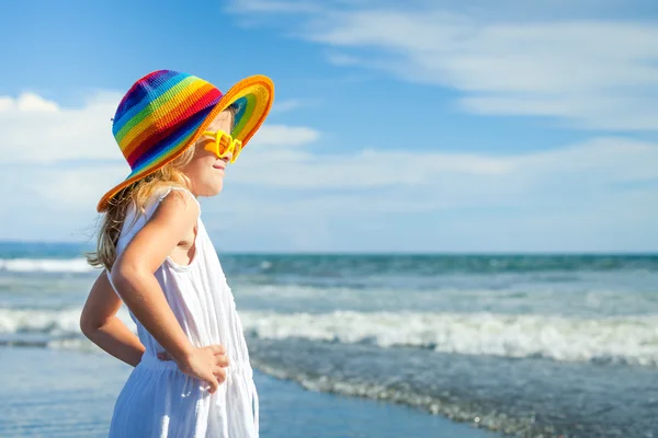 Glad liten tjej i hatt står på stranden i dag t — Stockfoto