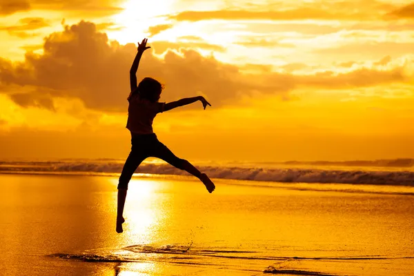 Glad tjej som hoppar på stranden på dawn tiden — Stockfoto