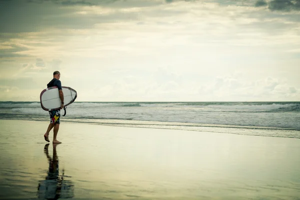 Sörfçü kurulu ile plaj boyunca yürür — Stok fotoğraf