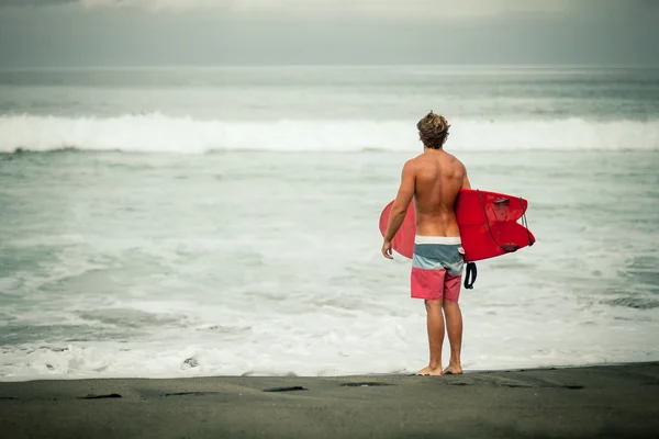 Surfista com prancha caminha ao longo da praia — Fotografia de Stock